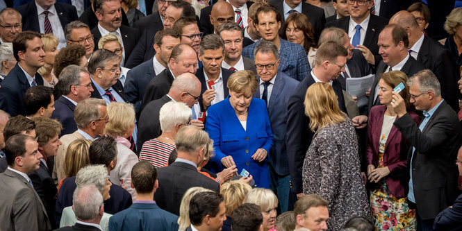 Viele Menschen stehen um eine Wahlurne herum. Sie halten Stimmkarten in der Hand