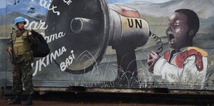 Ein Soldat steht an einem Wandbild. Darauf ist ein Junge abgebildet, der in ein Megafon "Frieden" schreit.