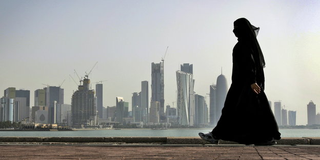 Eine verhüllte Frau spaziert vor der Skyline der Stadt Doha (Katar)