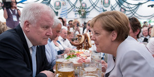 Angela Merkel und Horst Seehofer sitzen sich an einem Biertisch gegenüber und blicken grimmig