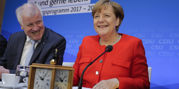 Seehofer und Merkel an einem Tisch mit Mikrofonen und einer Uhr