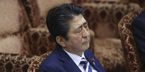Shinzo Abe sitzt mit geschlossenen Augen auf einem Stuhl