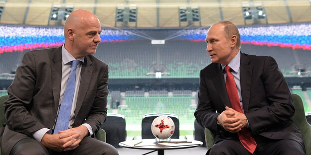 zwei Männer im Anzug sitzen in einem leeren Fußballstadion