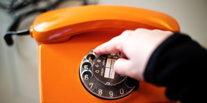 Eine Hand wählt an der Drehscheibe eines alten, orangefarbenen Telefons eine Nummer
