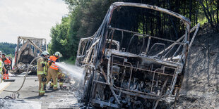 Feuerwehrleute löschen Brandreste an einem Autowrack