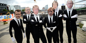 Sechs Menschen posieren mit Masken von Regierungschefs der G20-Länder