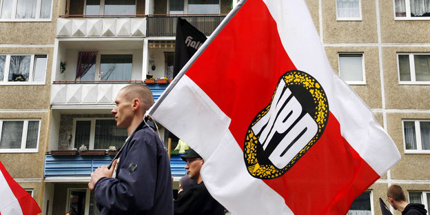 Ein Mann mit Glatze trägt eine NPD-Fahne