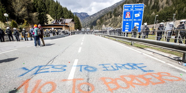Ein Autobahnteilstück umstellt von Polizisten in Montur, mit Kreide draufgeschrieben: „Yes to Europe, No to Borders“