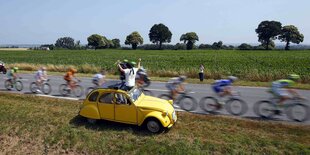 Ein Mann jubelt aus einem Auto vorbeifahrenden Radfahrern zu