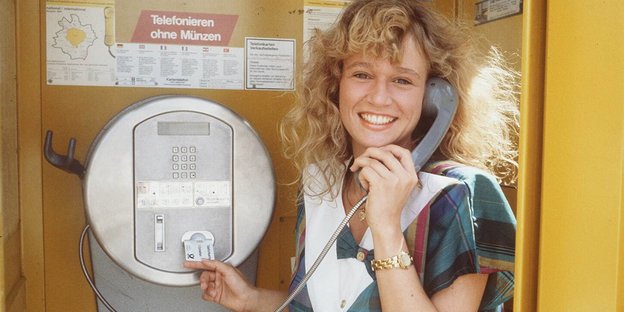 Eine Frau steht in einer Telefonzelle und steckt eine Telefonkarte in den Apparat
