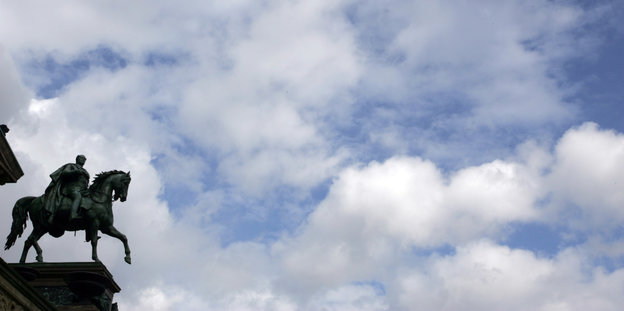 Vor weißen Wolken und einem blauen Himmel ragt eine Reiterstatue Wilhelms des IV. ins Bild