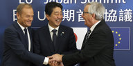 Donald Tusk, Shinzo Abe und Jean-Claude Juncker legen lächelnd ihre Hände übereinander