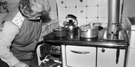 Eine Hausfrau schiebt mit einer Schaufel neue Kohle in ihren Ofen nach. Schwarzweiß-Bild von 1979.