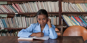 Ein Mädchen sitzt in einer Bibliothek und schaut von ihrem Buch hoch.