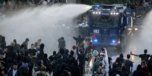 Ein Wasserwerfer spritzt auf schwarzbekleidete Demonstranten