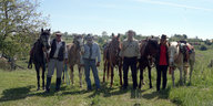 Fünf Pferde und vier Reiter posieren nebeneinanderstehend auf einer Wiese