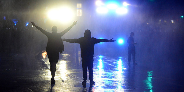 Zwei DemonstrantInnen stehen auf der nächtliche Straße vor zwei Wasserwerfern