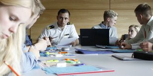 Schüler und ein Mann in Uniform arbeiten an einem Tisch