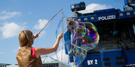 Vor einem Wasserwerfer macht eine Frau riesige Seifenblase