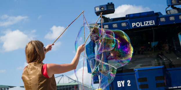 Vor einem Wasserwerfer macht eine Frau riesige Seifenblase