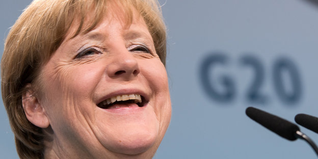 Angela Merkel lacht, im Hintergrund das G20-Logo
