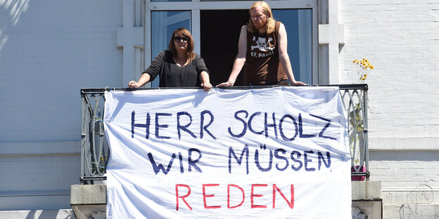 Zwei Menschen stehen auf einem Balkon, vor ihnen ein Schild, auf dem steht: Herr Scholz wir müssen reden