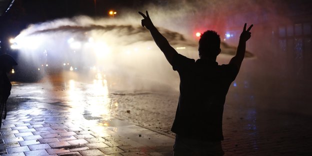 Ein Demonstrant steht im Scheinwerferlicht eines Wasserwerfers