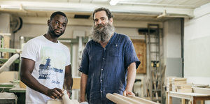 Zwei Männer stehen in einer Werkstatt, ernst in die Kamera schauend