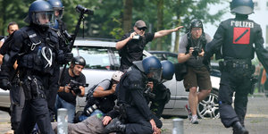 Polizisten drücke einen Menschen zu Boden daneben steht ein gestikulierender Journalist