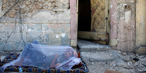 ein Mann schläft unter einem Moskitonetz vor einer Haustür auf einer Matratze