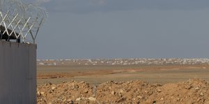 Blick auf die Behausungen des Flüchtlingslagers in der Ferne, rechts im Bild eine Mauerecke mit Stacheldraht