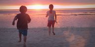Zwei Kinder laufen Richtung Sonnenuntergang