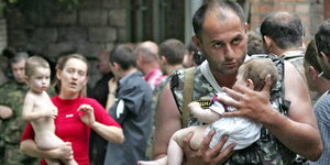 Ein Soldat und eine Frau tragen Kinder auf dem Arm, sie blicken schockiert
