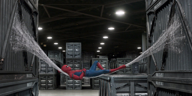 Spider-Man, Superheld im Spinnenkostüm, in einer Hängematte aus Spinnenfäden zwischen zwei Containern.