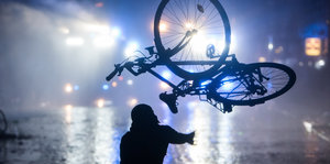 Eine Person wirft im Hamburger Schanzenviertel ein Fahrrad in Richtung von Wasserwerfern