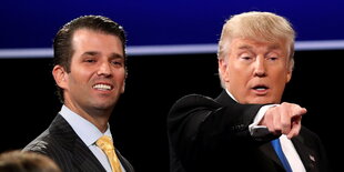 Donald Trump jr. grinst neben seinem Vater Donald Trump, der irgendwohin zeigt