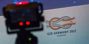 Eine Kamera steht vor einer Wand mit dem Logo des G20-Gipfel.