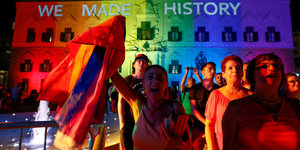 Menschen mit Regenbogenfahnen vor einem beleuchteten Gebäude