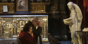 Ein älteres Ehepaar, Frau und Mann, betet vor einer Heiligenfigur