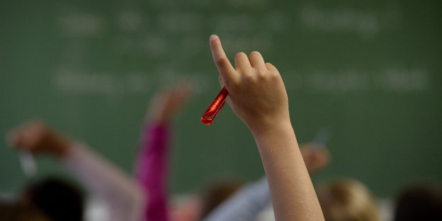 Eine zum Melden in die Luft gestreckte Kinderhand in einem Klassenzimmer
