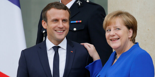 Emmanuel Macron und Angela Merkel stehen vor Flaggen