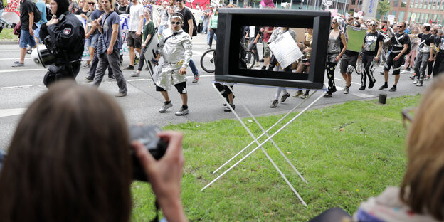 Eine Person fotografiert durch einen alten Fernseher eine Anti-G20-Demo