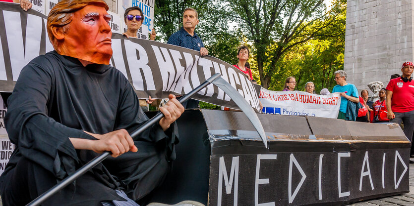 Ein Demonstrant trägt eine Trump-Maske eine schwarze Kutte. Er hält eine Sichel in der Hand