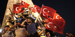 Männer halten türkische Flaggen vor einem Monument in die Höhe