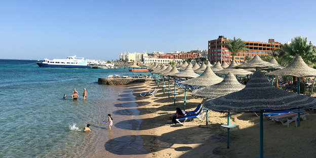 Ein Strand mit Sonnenschirmen. Links das Wasser, im Hintergrund die Silhouette des Ortes