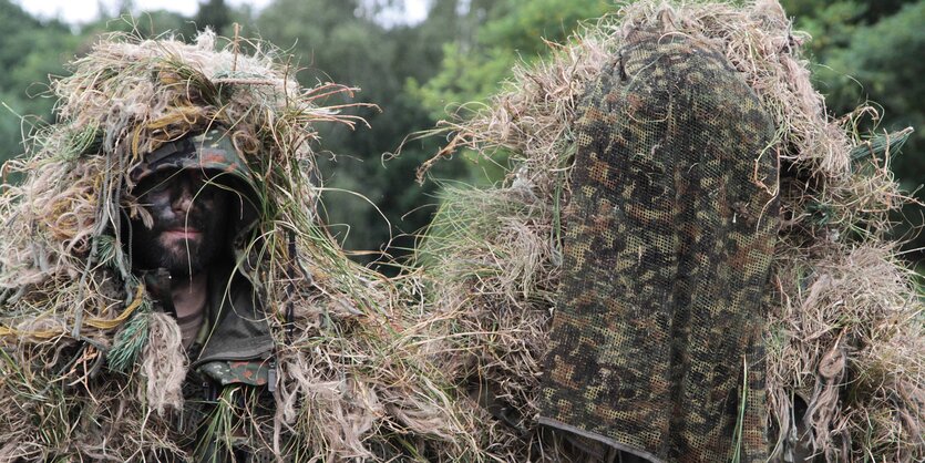 Zwei Soldaten getarnt durch Kleidung und Stroh, der linke Soldat hat sein Gesicht geschwärzt