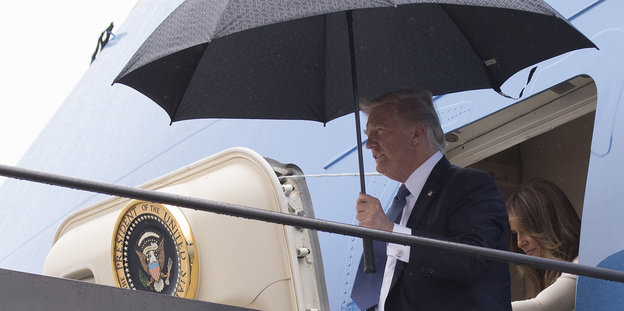 Ein Mann hält einen Regenschirm, während er aus einem Flugzeug steigt