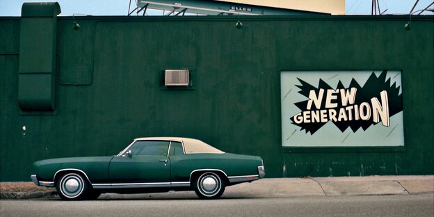 Ein grünes Auto steht vor einer grünen Wand, an der ein Werbeplakat mit der Aufschrit „New Generation“ hängt