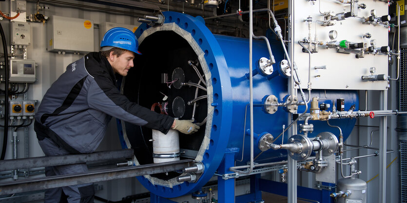 Ein Mann mit Helm beuht sich über ein technisches Gerät, das aus einer blauen Röhre ragt