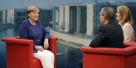 Angela Merkel sitzt in einem roten Sessel, gegenüber von Thomas Baumann und Tina Hassel